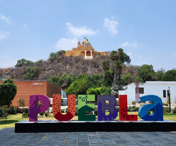       Colorful 'PUEBLA' sign with a hilltop church in the background.
  