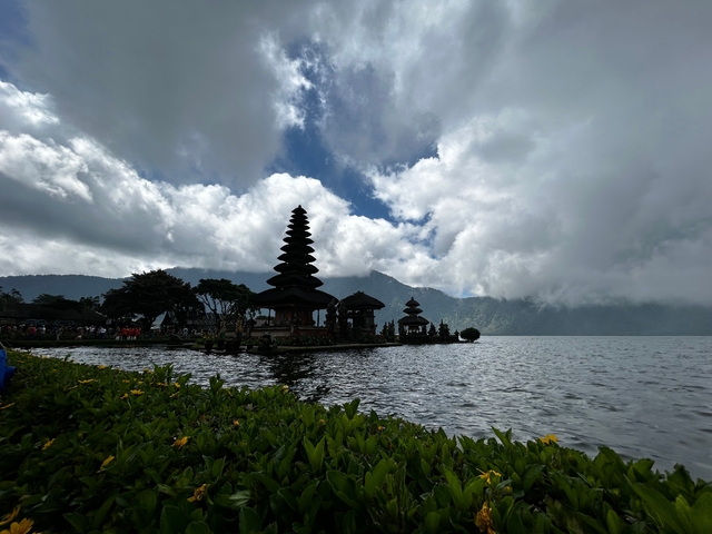 Temple by a lake surrounded by mountains and clouds.