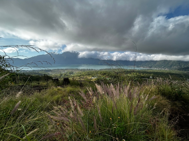 View of a lush valley with a distant lake and clouds.