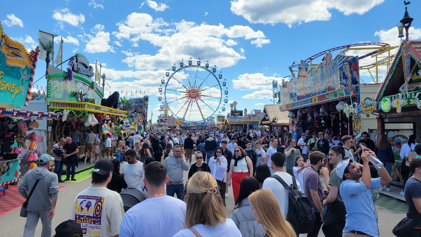 Crowded festival with fair rides under a clear sky.
