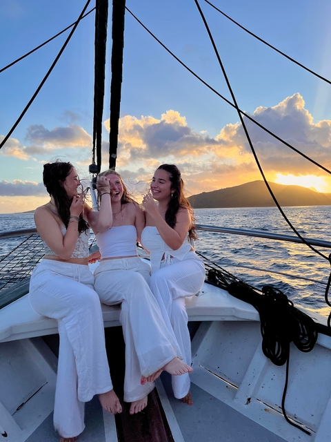 Three women on a sailboat at sunset, smiling.