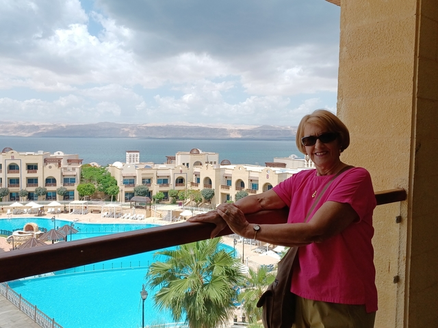 A person enjoying a view from a balcony overlooking a pool and the sea.