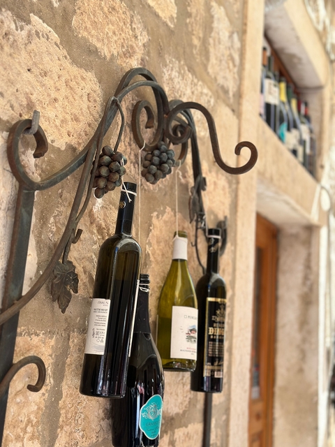 Wine bottles hanging on a rustic metal holder with grapes.