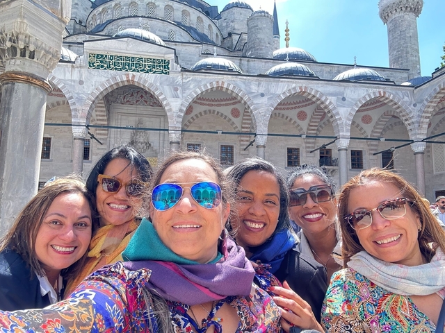 Smiling women in front of a grand mosque.