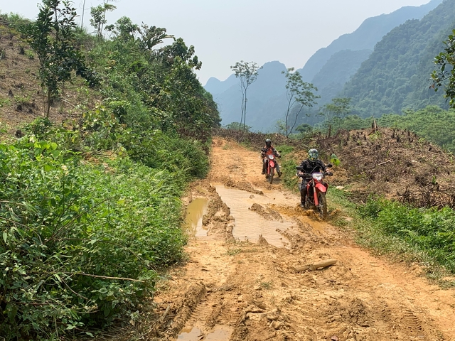 Motorcyclists traversing a muddy rural path.