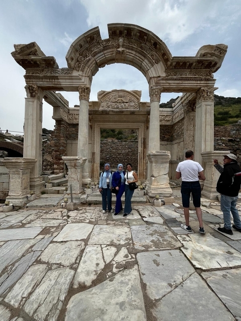 Three women and a man stand in front of ancient Roman-style ruins with columns.