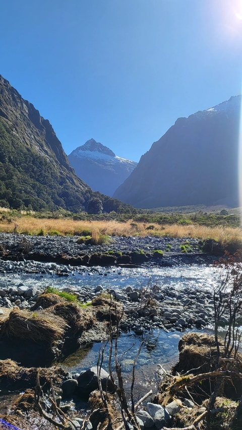       A scenic view of mountains and a river under a clear sky.
  