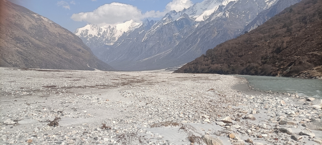 A scenic view of a valley with snowy mountains in the background and a rocky riverbed.