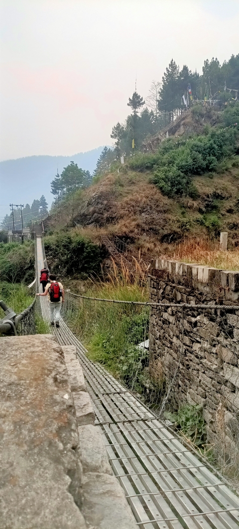 Two people walking on a suspension bridge in a hilly area.