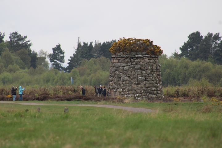       Landscape with a stone cairn and people at Culloden Battlefield.
  