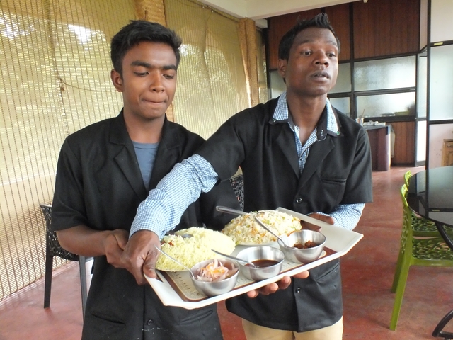       Two waiters serving traditional Indian meals on trays.
  