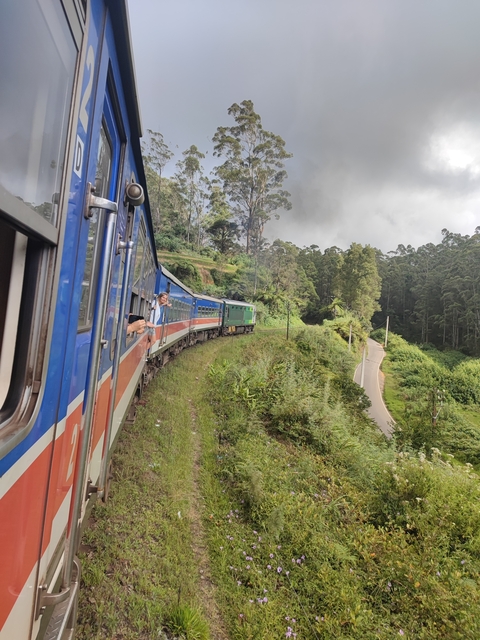 A train journey through a lush green landscape with passengers leaning out.