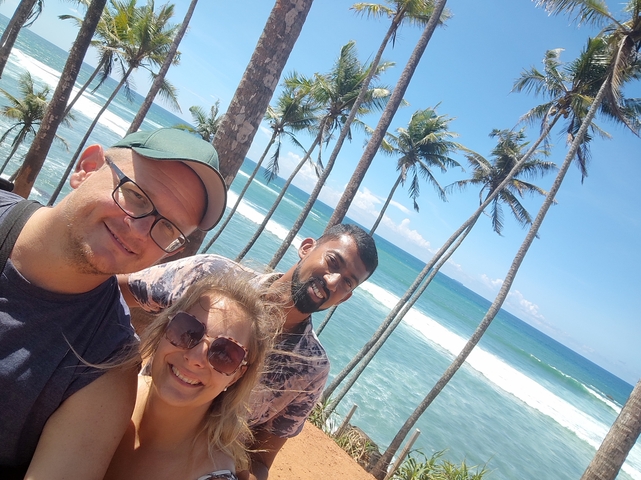 Three people posing by palm trees and ocean.