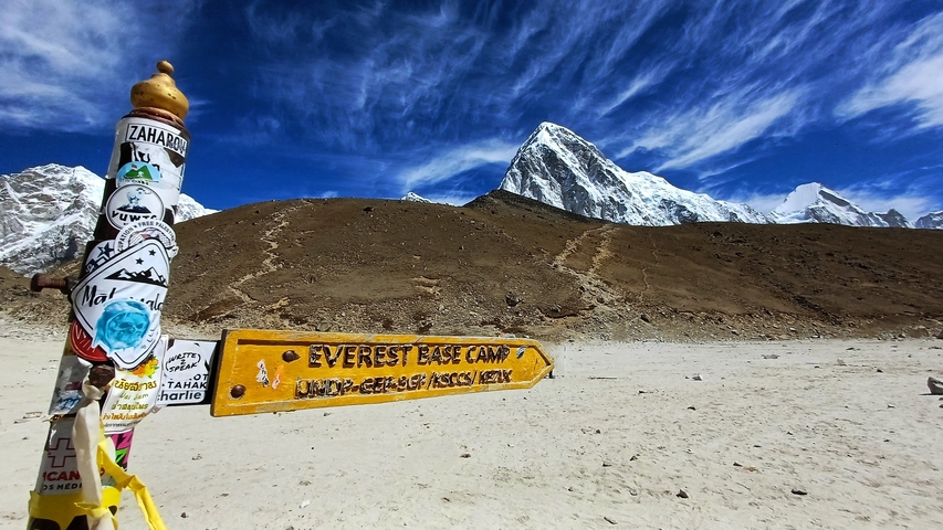 Everest Base Camp sign with mountains in the background.