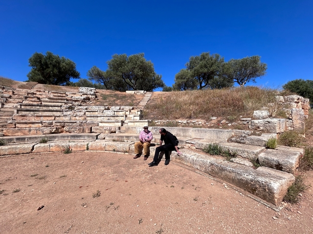 Two people sitting in an ancient amphitheater under a clear sky.