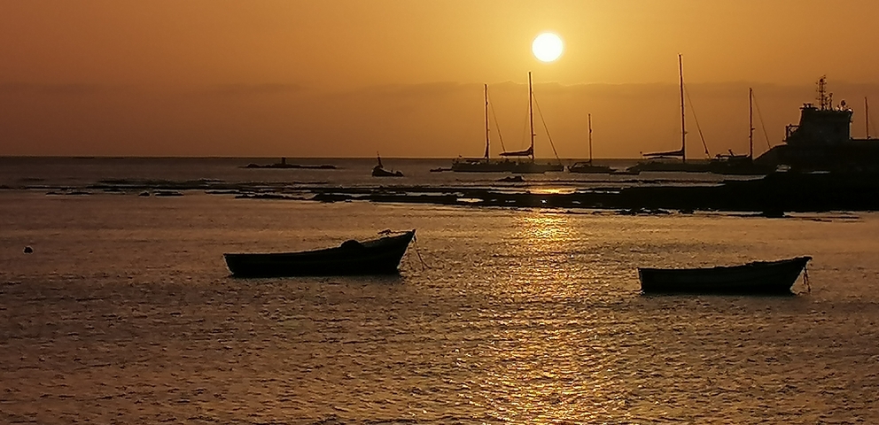 Sunset over the sea with silhouetted boats.