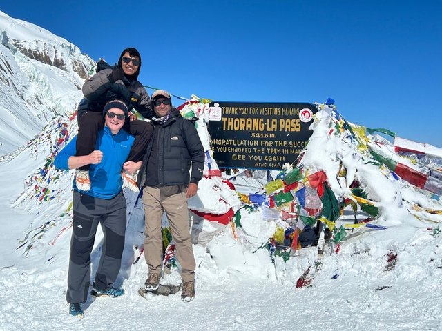 Three people standing at the Thorong La Pass with snow-covered surroundings