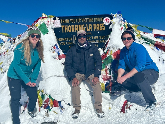 Three people at Thorong La Pass posing in front of a sign and snow