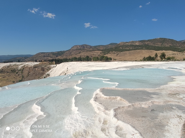       White travertine terraces with turquoise pools.
  
