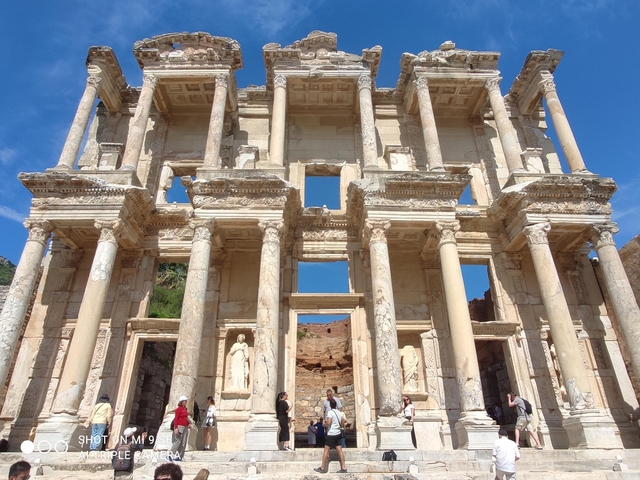       Historic library ruin with statues, with tourists exploring.
  