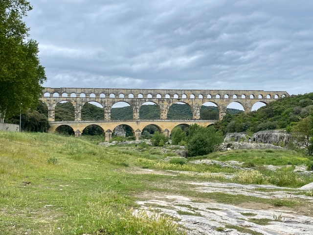       Ancient Roman aqueduct surrounded by greenery under a cloudy sky.
  