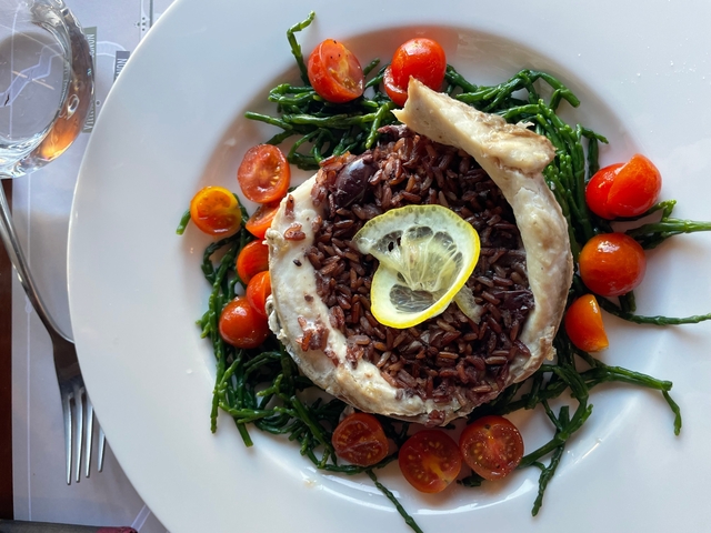       Gourmet dish with fish, rice, and vegetables under natural light.
  