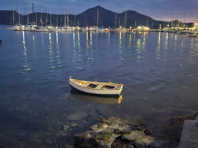 A serene harbor with boats lit at night and a lone rowboat in the foreground.