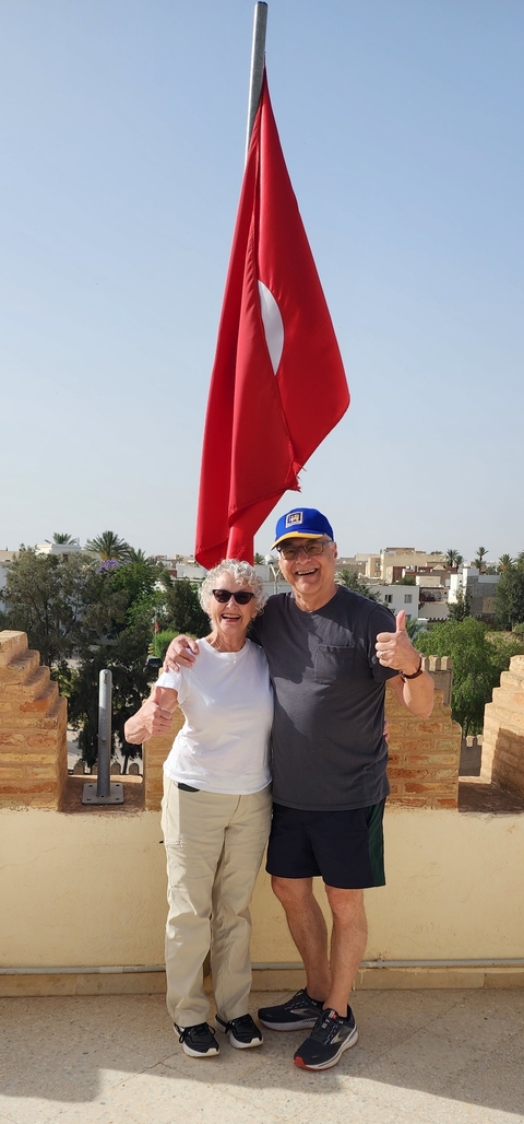 Smiling couple posing with a cityscape and flag in the background.