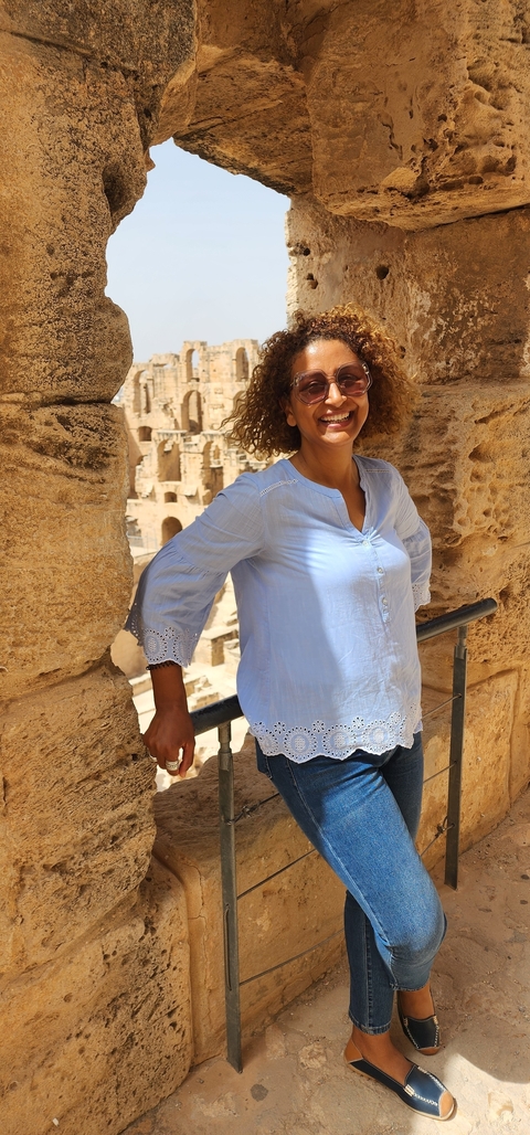 Smiling person standing against ancient stone architecture.