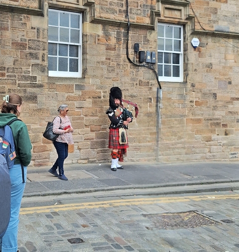       Person in traditional Scottish attire playing bagpipes on a street.
  