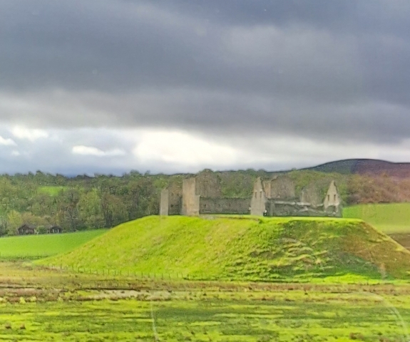 Blurry view of a historic stone structure on a grassy hill.