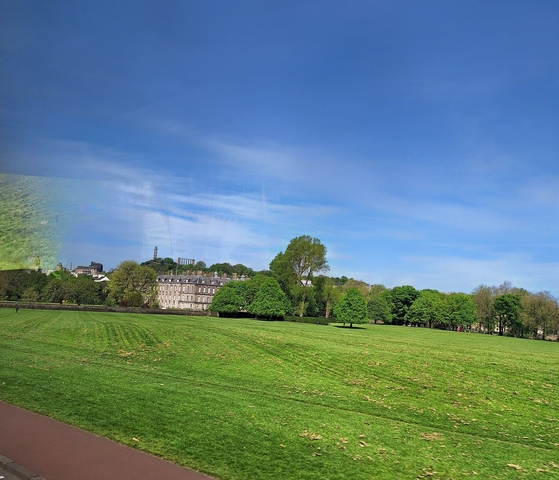 Wide view of a grassy field with trees and buildings.