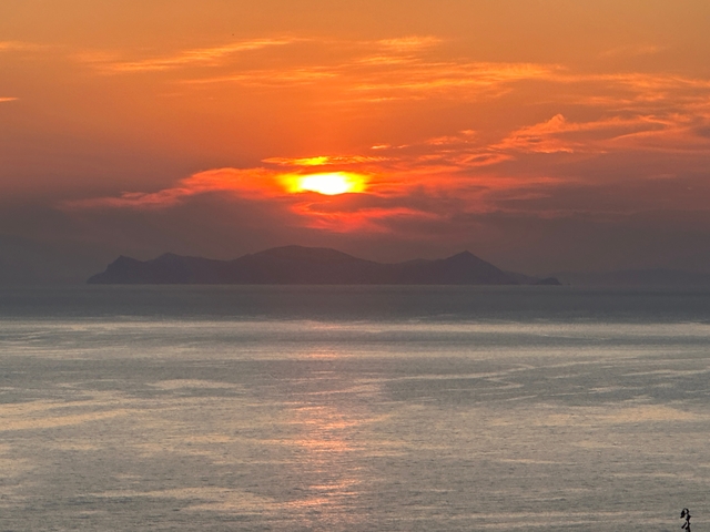       Sunset over the sea with an island silhouette.
  