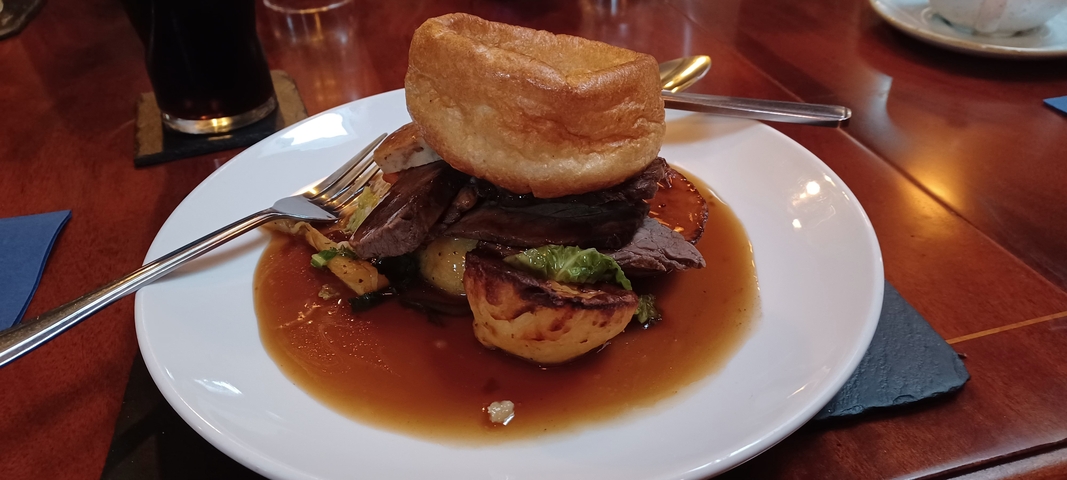 Plated dish with sliced meat and vegetables, topped with a Yorkshire pudding.