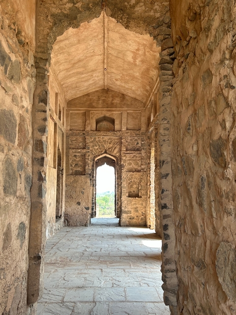 Stone corridor with arched openings and distant landscape view.
