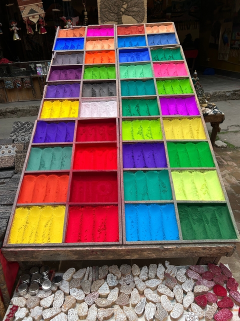 Colorful powders displayed in wooden compartments on a street.