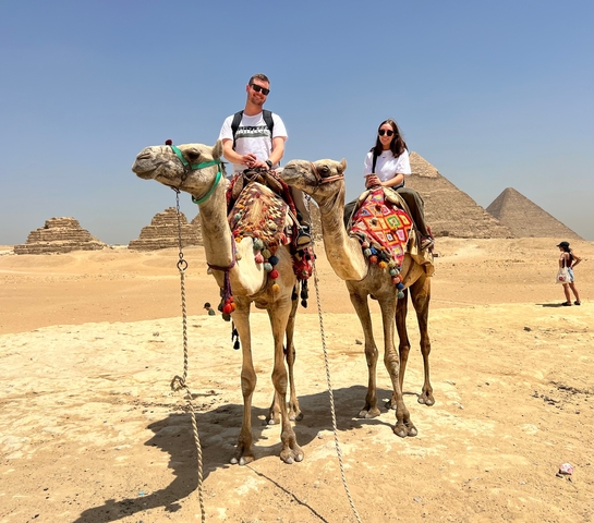 Tourists riding camels in front of the Pyramids of Giza.