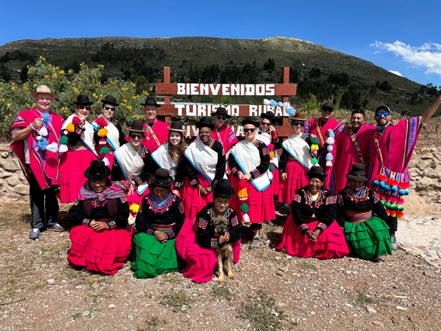       Group of people in traditional attire posing by a welcome sign.
  