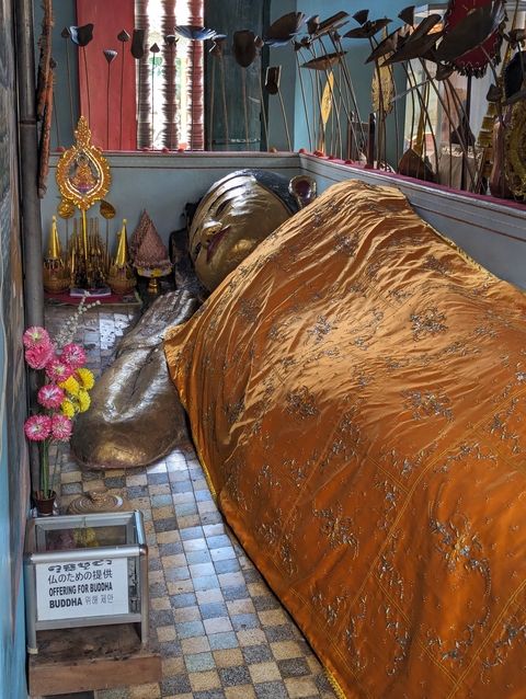 A reclining Buddha statue covered with ornate fabric.