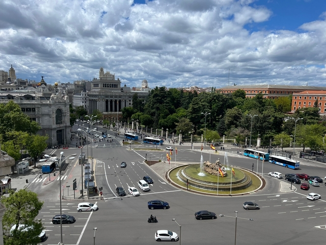       City square with a fountain and traffic, surrounded by historic buildings.
  