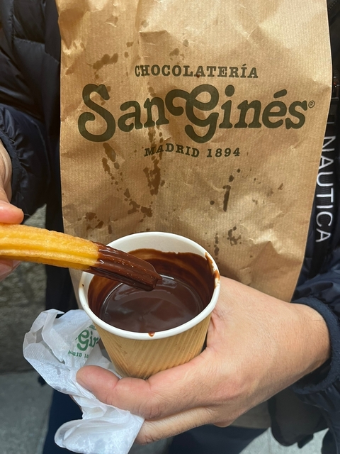       Person holding a churro dipped in chocolate with a takeout cup.
  