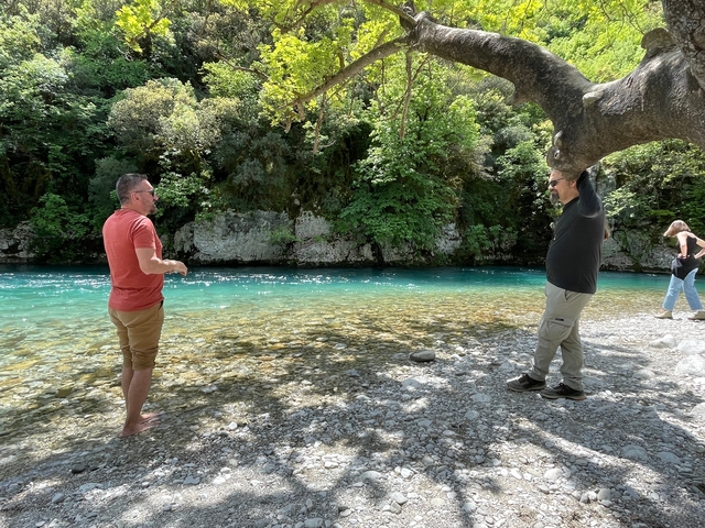       People standing by a blue river surrounded by greenery.
  