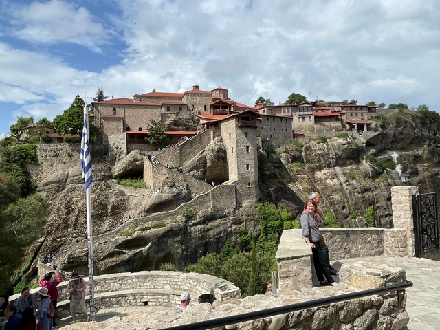      Monastery complex on rock formations with a Greek flag.
  