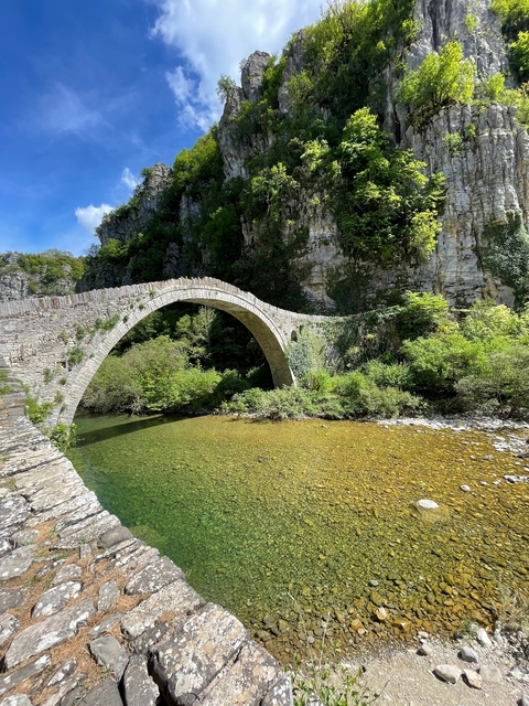       Stone arch bridge over a clear river surrounded by lush vegetation.
  