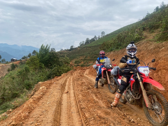 Motorcyclists on a muddy trail in a hilly landscape