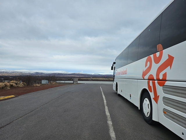 Tour bus parked with a scenic view of the Icelandic landscape with mountains in the background.