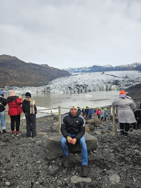 Tourists exploring a glacier with a large body of water and mountains in the background.