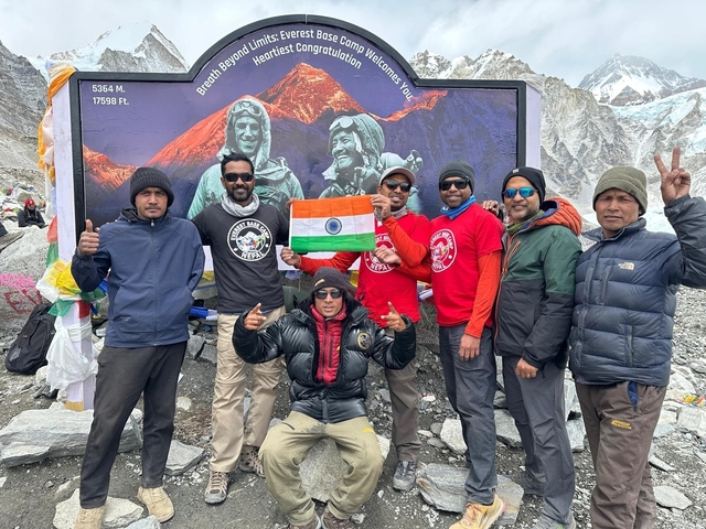      A group of people in front of a mural holding a flag, celebrating at a snowy mountain location.
  