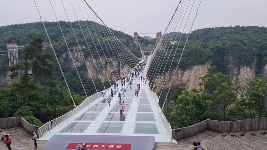 People walking on a glass bridge surrounded by cliffs.