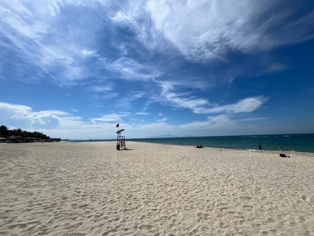 Long sandy beach with few visitors and lifeguard post.